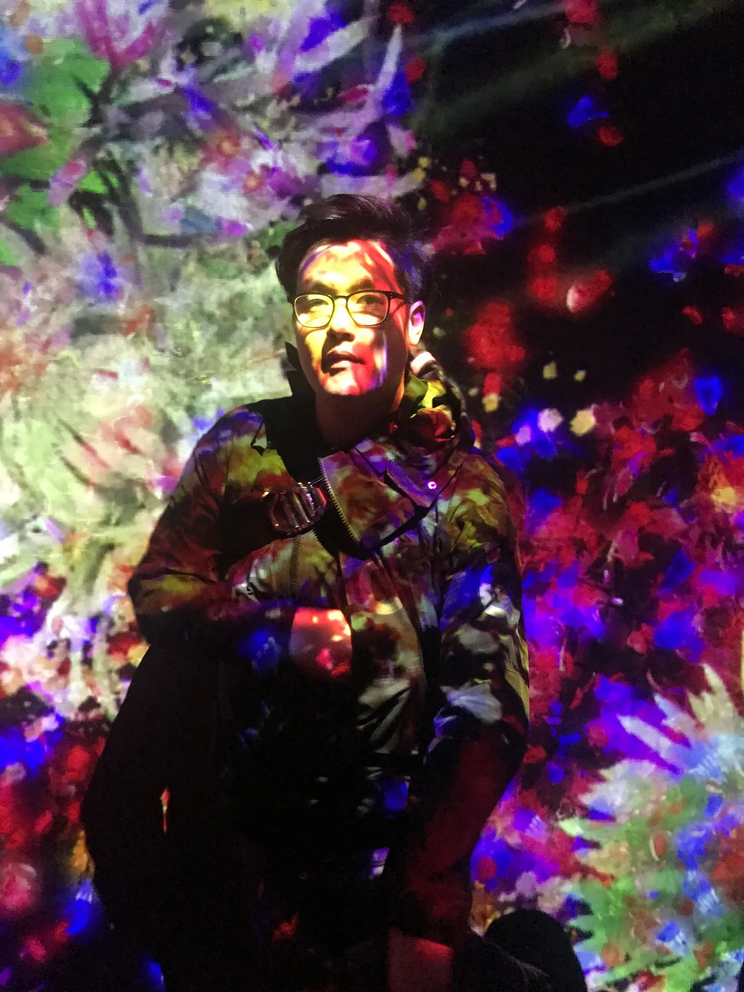 Kevin Deng, lit by a room of projected flowers.